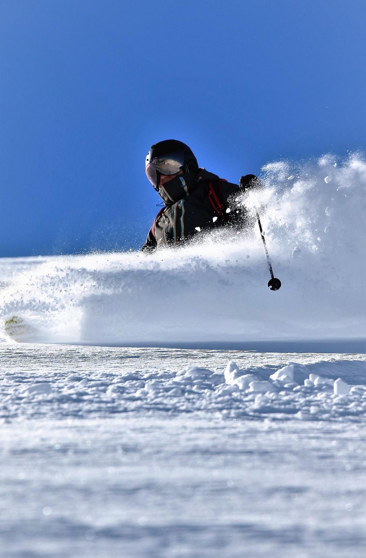 Skier carves through deep powder snow on a bright blue day.