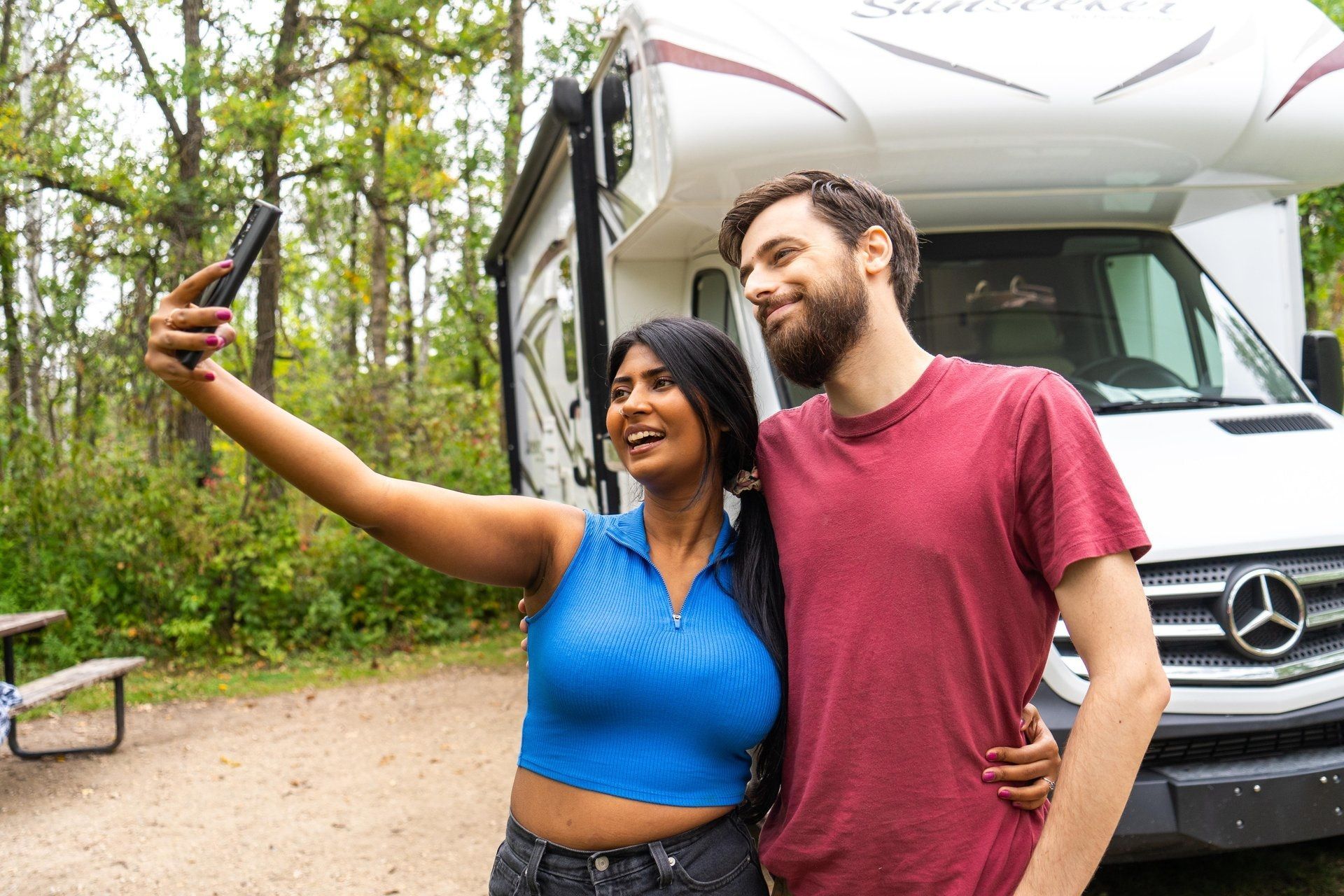 @Handcraft Courtesy of Travel Manitoba Een stel maakt een selfie voor een camper. Ze glimlachen in een bosrijk gebied.