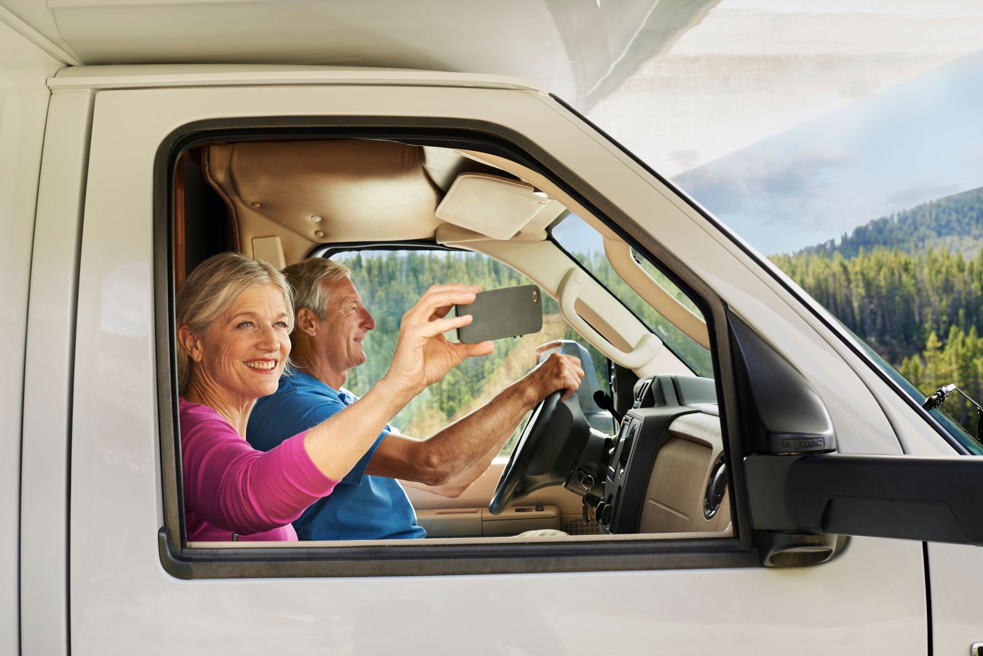 @Travel Alberta / Anthony Redpath Een stel in een camper maakt een selfie met een schilderachtig berglandschap op de achtergrond.
