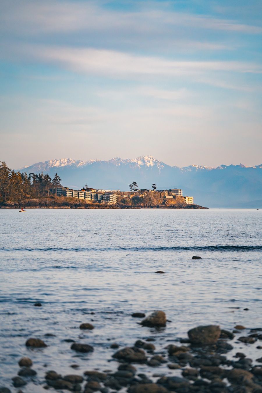 Oceaankustlijn met gebouwen, bergen op de achtergrond onder een blauwe hemel.