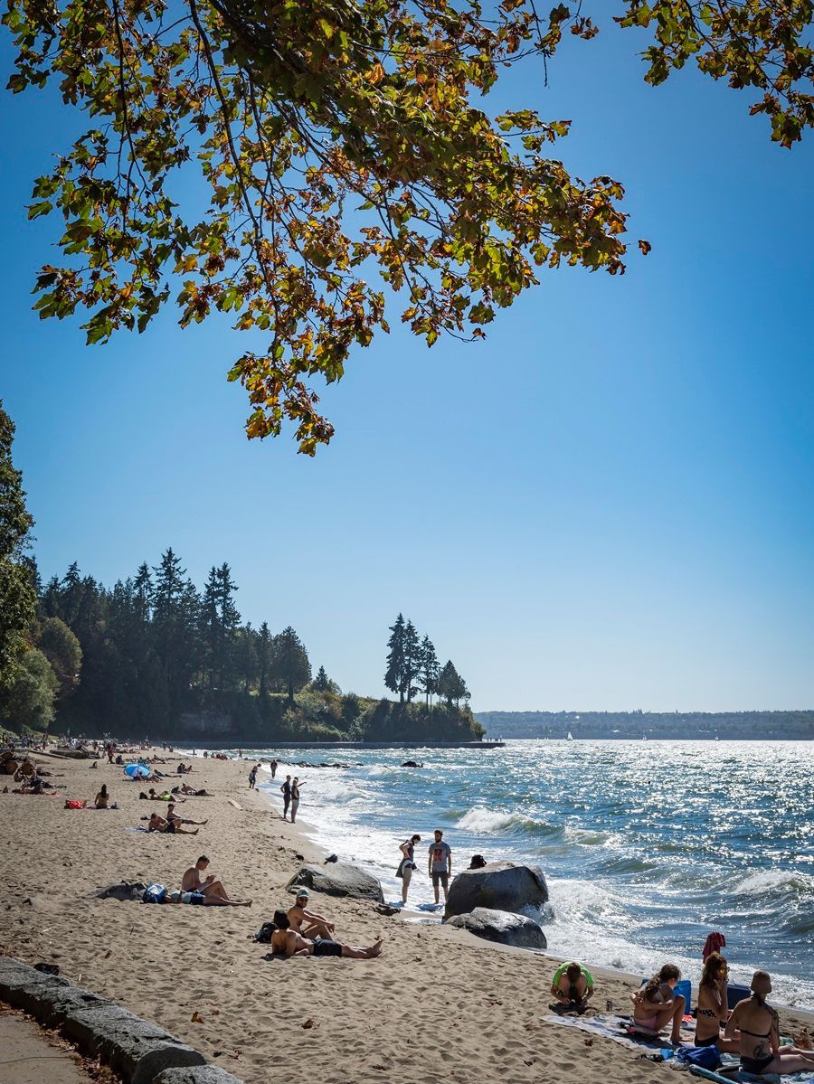 © Jiri Saftar Strandtafereel met mensen die zonnebaden en langs het water wandelen op een zonnige dag.