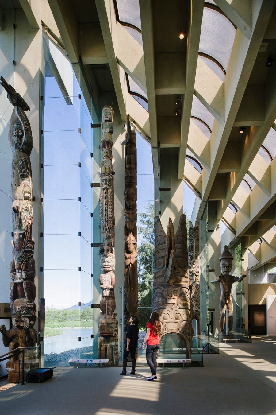 @Destination Canada Interieurbeeld van een museum met diverse totempalen in de tentoonstelling. Twee personen staan ​​bij een centrale paal.