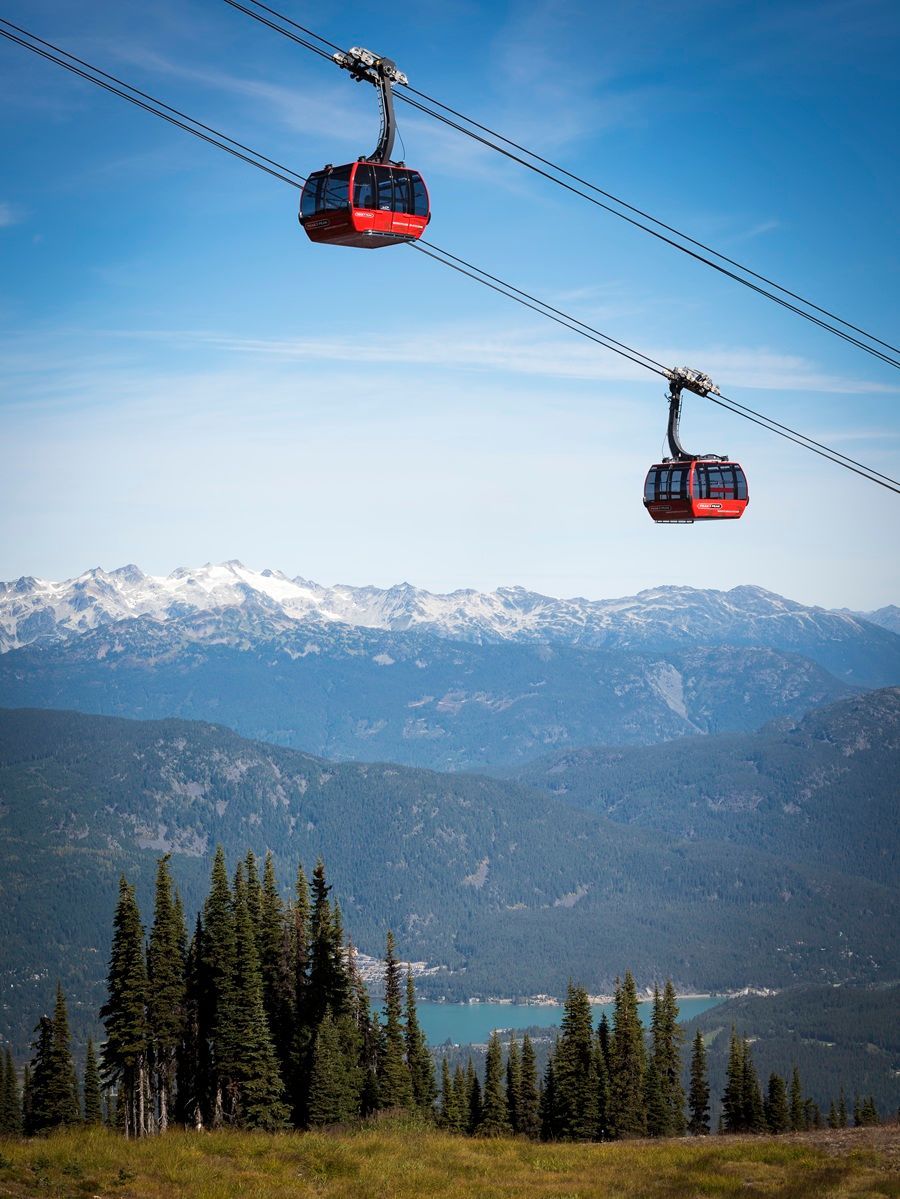 © Jiri Saftar Rode gondels die over een berglandschap met besneeuwde toppen en een blauwe hemel rijden.