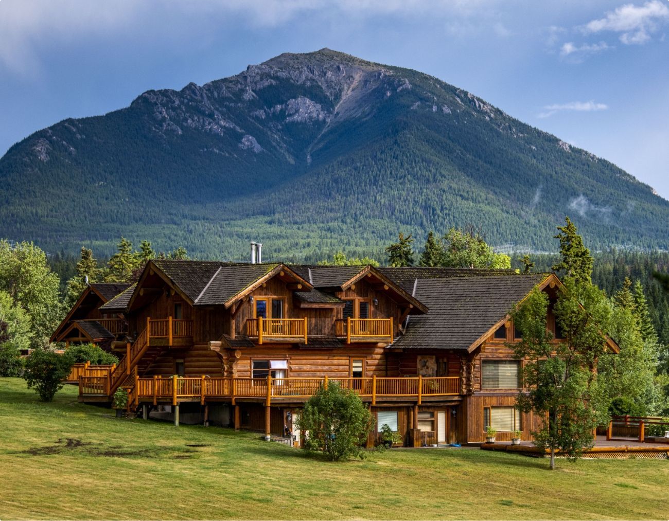 Echo Valley Ranch met groen gazon, gelegen voor een beboste bergtop onder een heldere hemel.