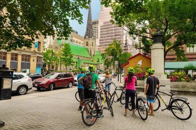 Fietsers verzamelden zich in een stadsstraat met geparkeerde auto's en hoge gebouwen op de achtergrond.