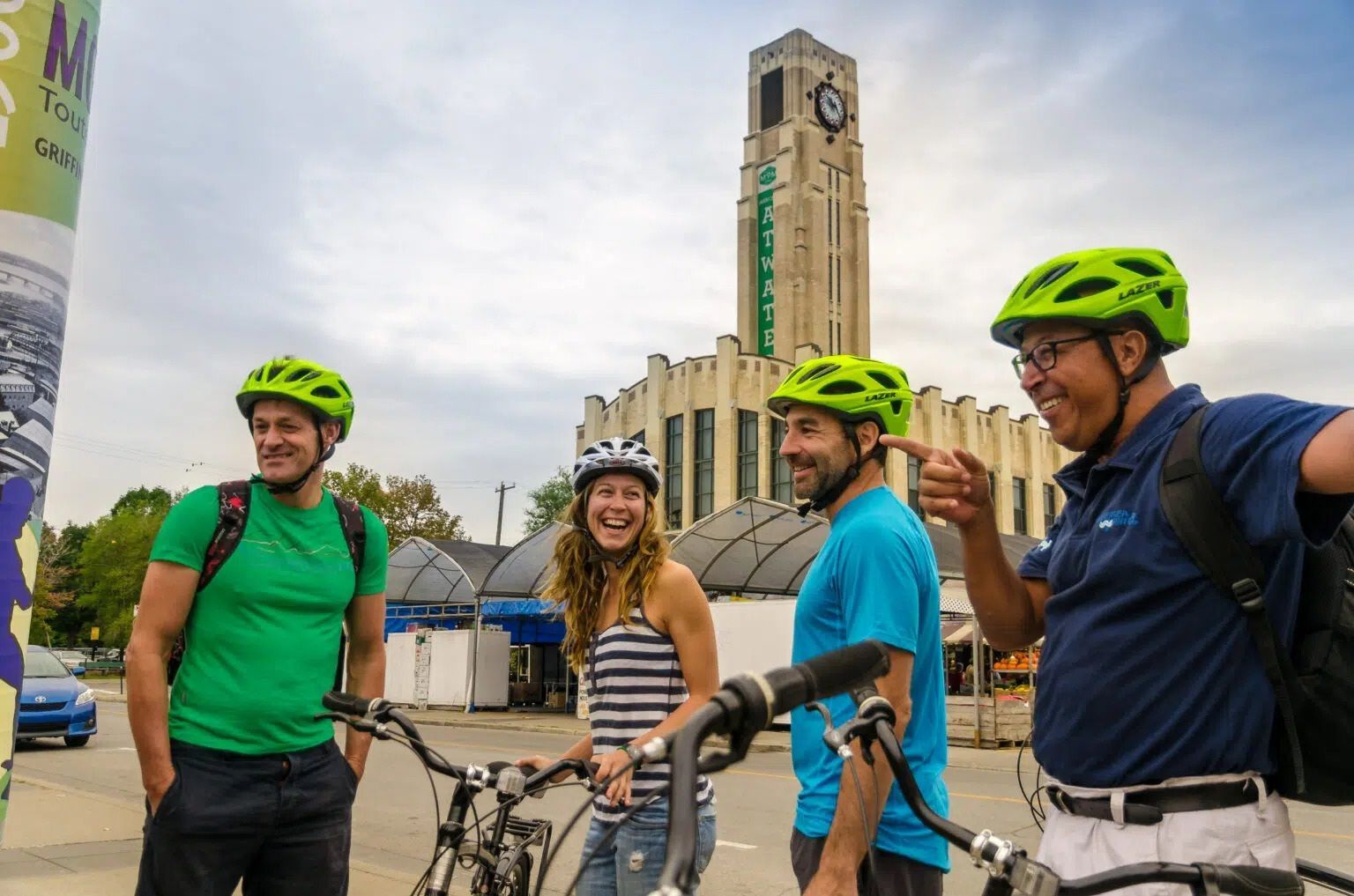 Vier fietsers met felgroene helmen poseren in Montréal met hun fietsen voor een hoge stadstoren.