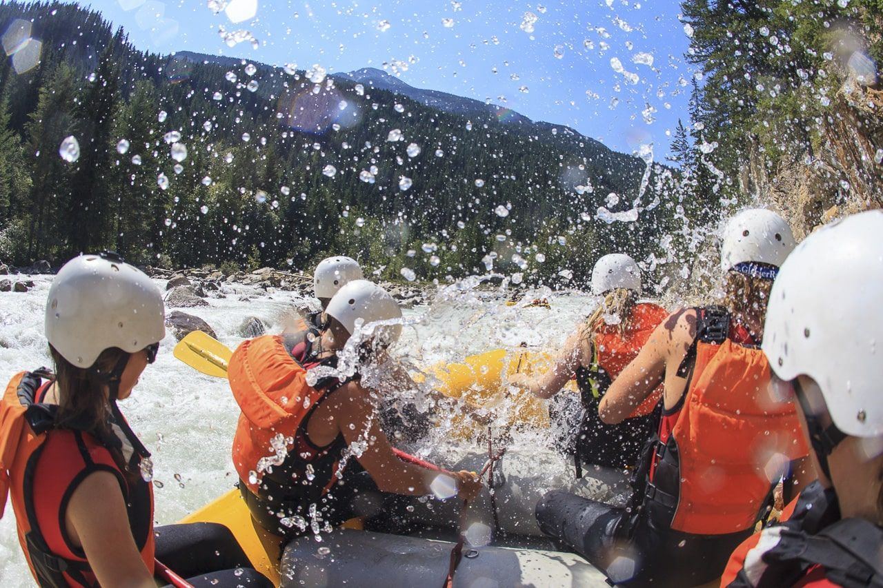 Wildwaterrafters in oranje reddingsvesten en witte helmen ploeteren door ruige stroomversnellingen onder een blauwe hemel.