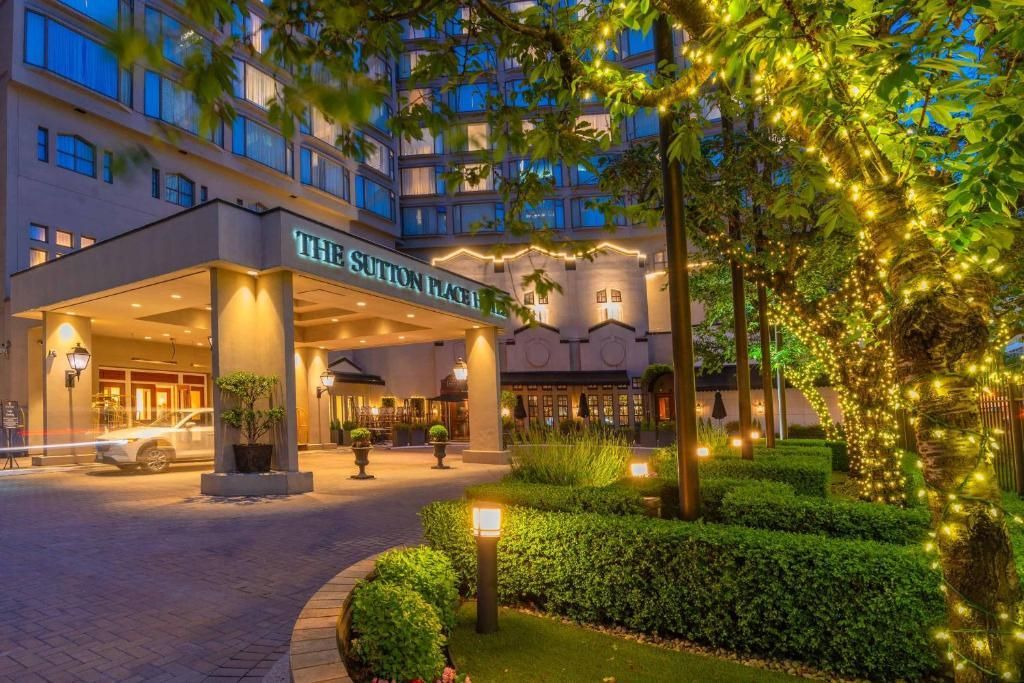 Verlichte hotelingang met palmbomen, verlichte ramen en een gebogen oprit bij schemering.