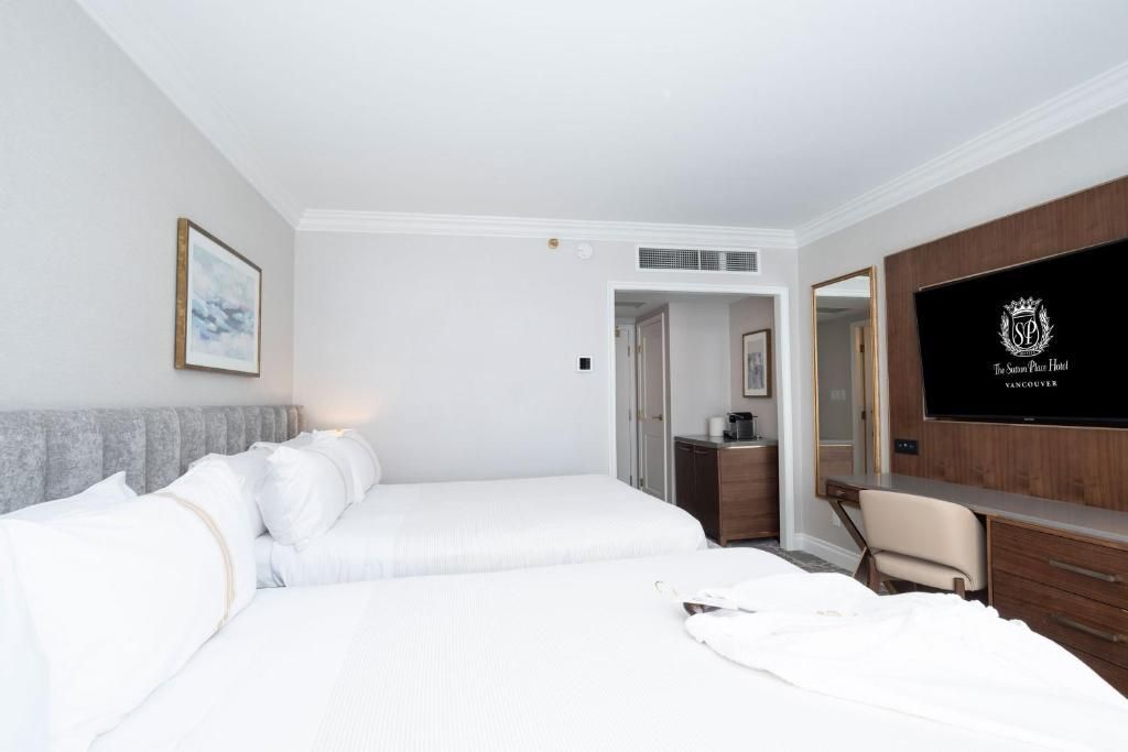 Lichte, moderne hotelkamer met twee witte bedden, tv, bureau en neutrale inrichting.