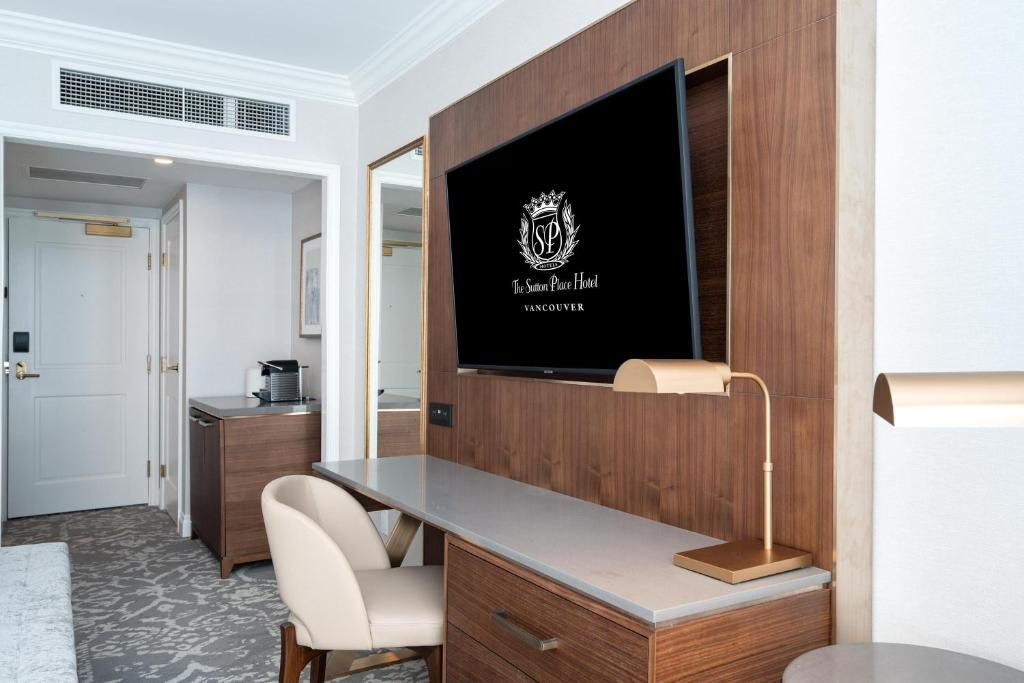 Hotelkamer met bureau, stoel, spiegel en aan de muur gemonteerde tv in een modern interieur met houten lambrisering.
