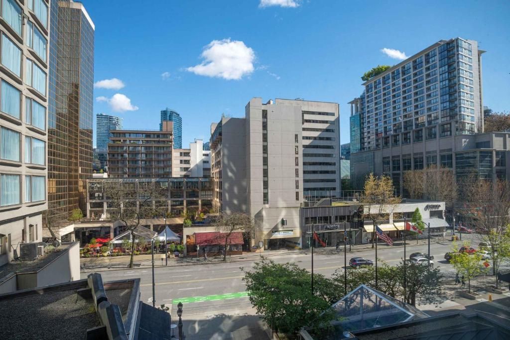 Stadsplein met moderne gebouwen, bomen en een helderblauwe lucht.