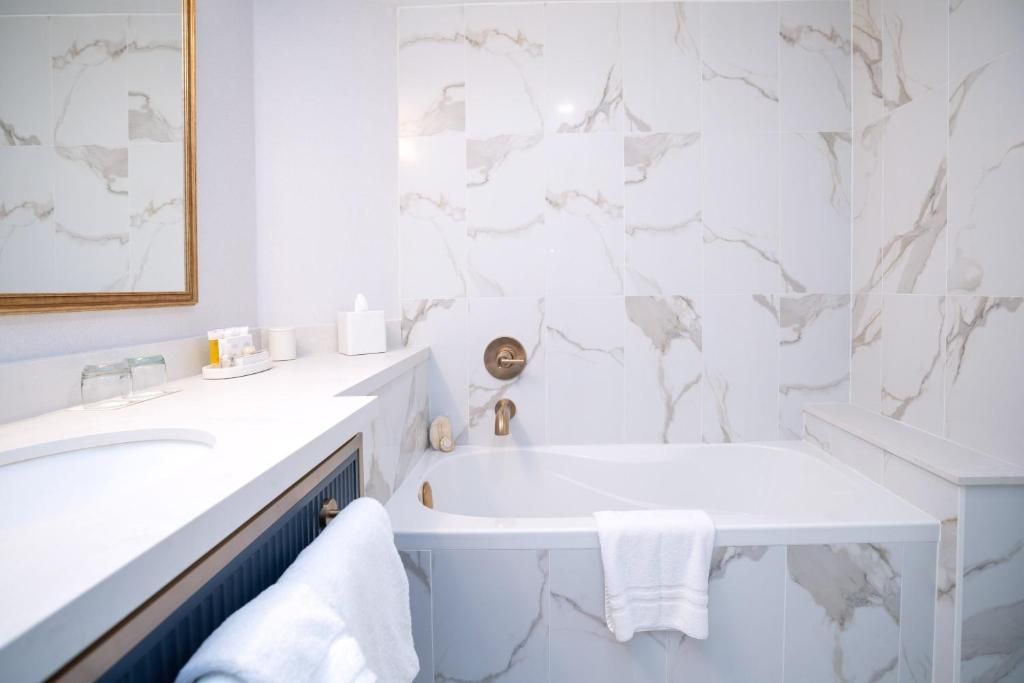 Lichte, moderne badkamer met witte marmeren muren, een groot bad en een wastafelmeubel met spiegel en handdoek.