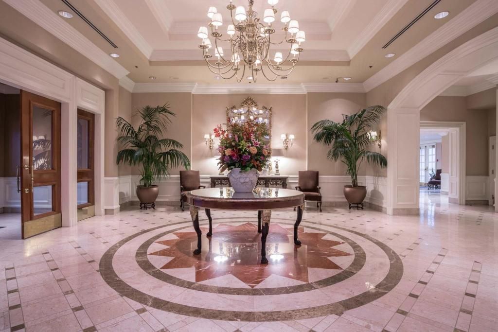 Elegante hotellobby met kroonluchter, marmeren vloer, ronde tafel en bloemstuk in het midden.