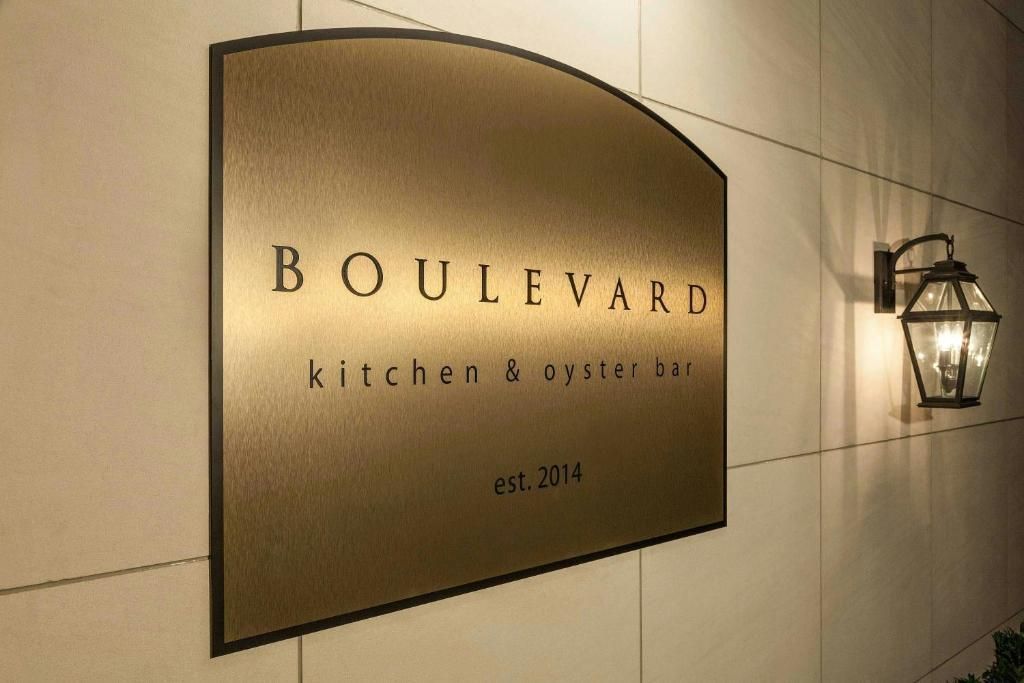 Het uithangbord van Boulevard Kitchen & Oyster Bar hangt aan een beige muur naast een lantaarnvormige lamp.