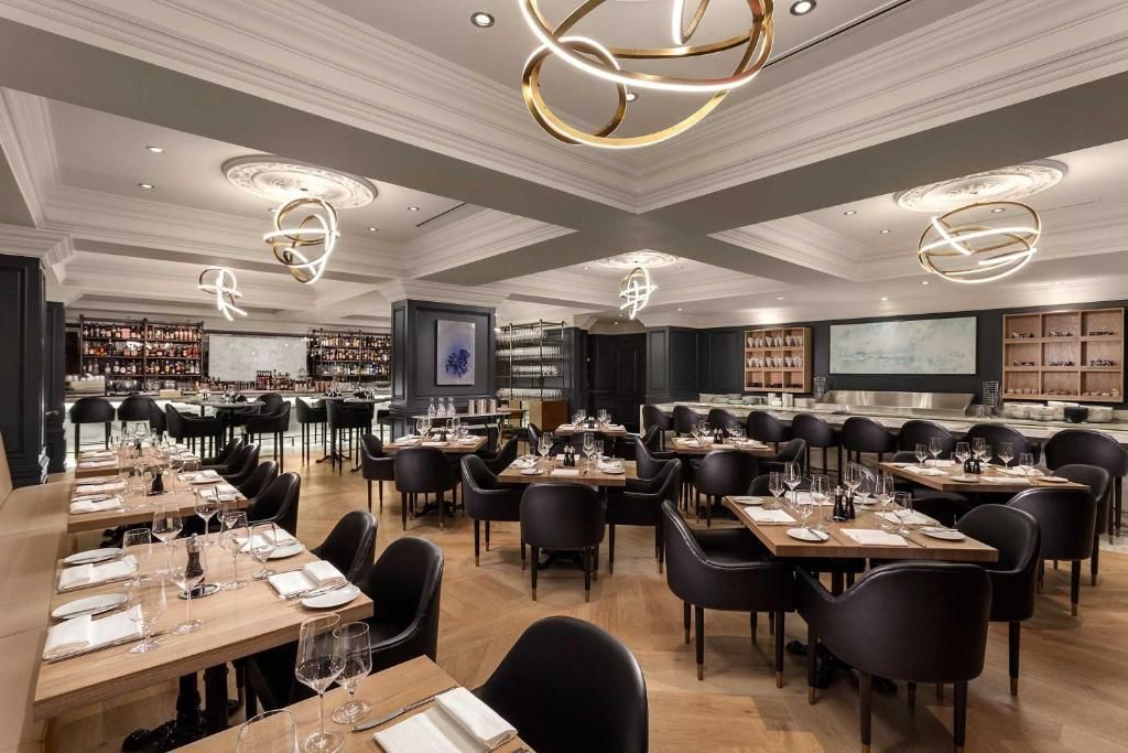 Een elegante, stijlvolle restaurantzaal met gedekte tafels, zwarte stoelen en sfeervolle kroonluchterverlichting.