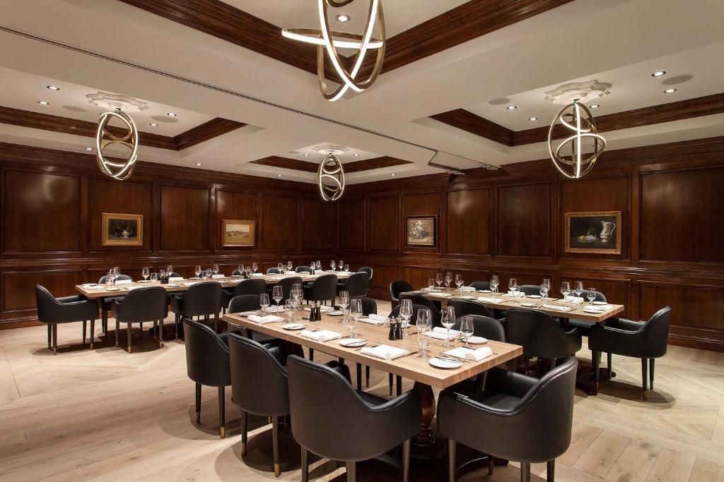 Een elegante restaurantzaal met gedekte tafels, zwarte stoelen, houten lambrisering en moderne hanglampen.