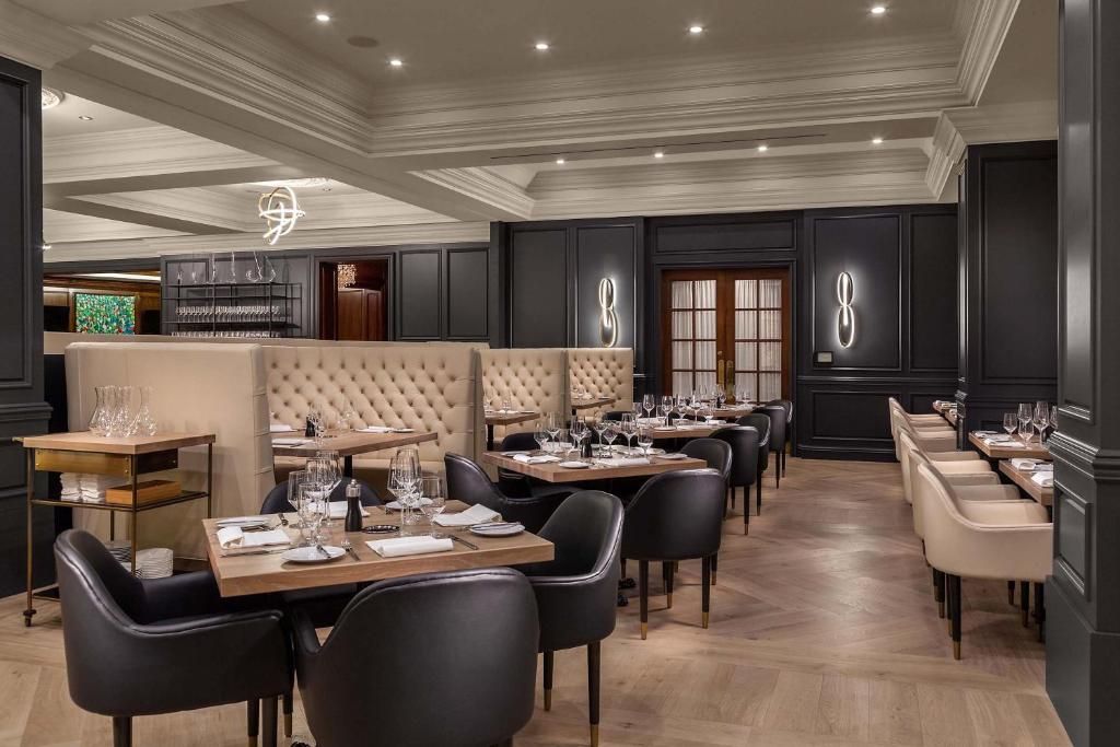 Een elegante, lege restaurantzaal met donkerhouten interieur, gecapitonneerde banken en keurig gedekte tafels.