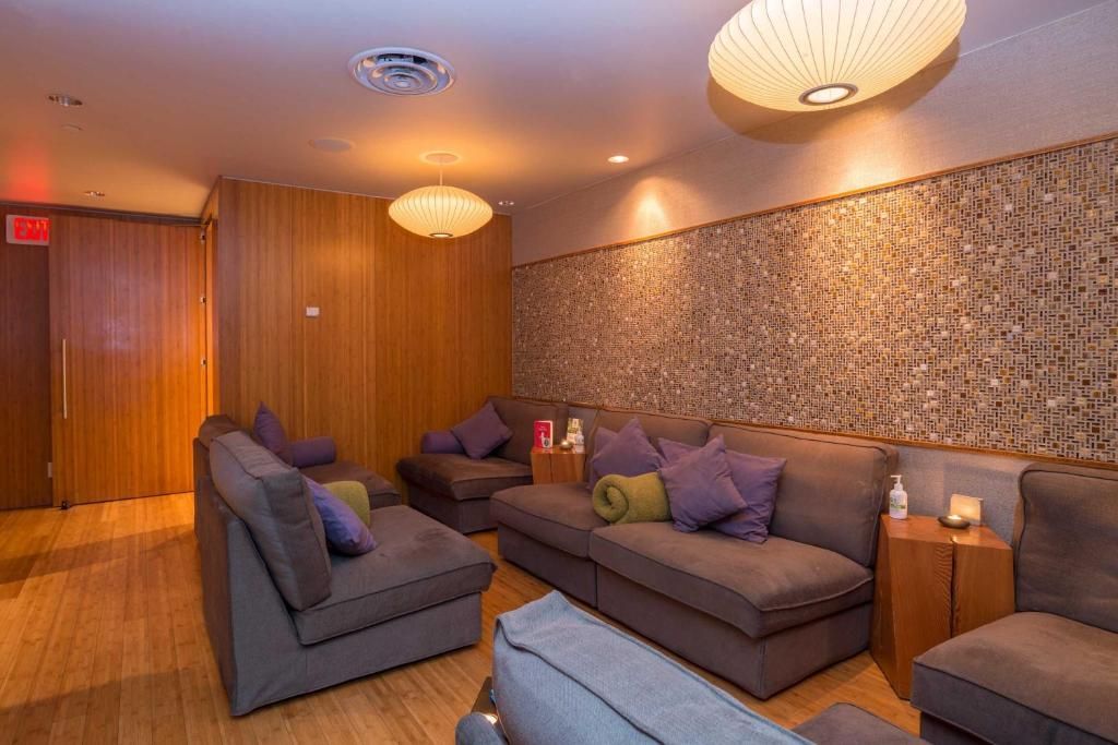 Gezellige lounge met bruine banken, paarse kussens, houten wanden en warme hanglampen.