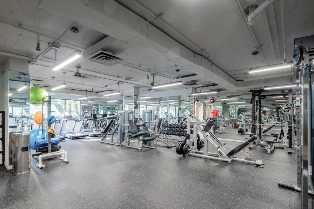 Licht en ruim interieur van de sportschool met fitnessapparaten en spiegels onder witte plafondlampen.