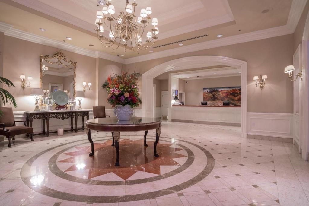 Elegante hotellobby met kroonluchter, marmeren vloer, ronde tafel als middelpunt en wandlampen.