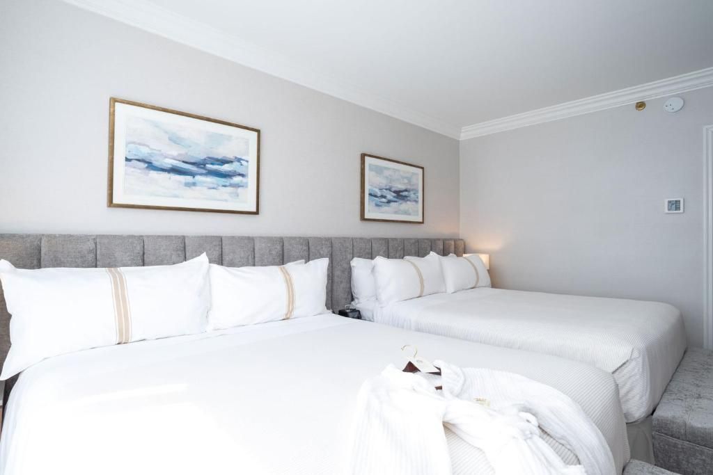 Lichte hotelkamer met twee witte bedden, een grijze accentmuur en ingelijste landschapsschilderijen.