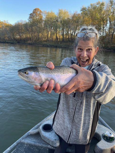 Woman in a boat holding a rainbow trout, river in the background, smiling.