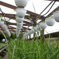 Rows of white hanging planters suspended in a wooden structure above a field of lush green grass.