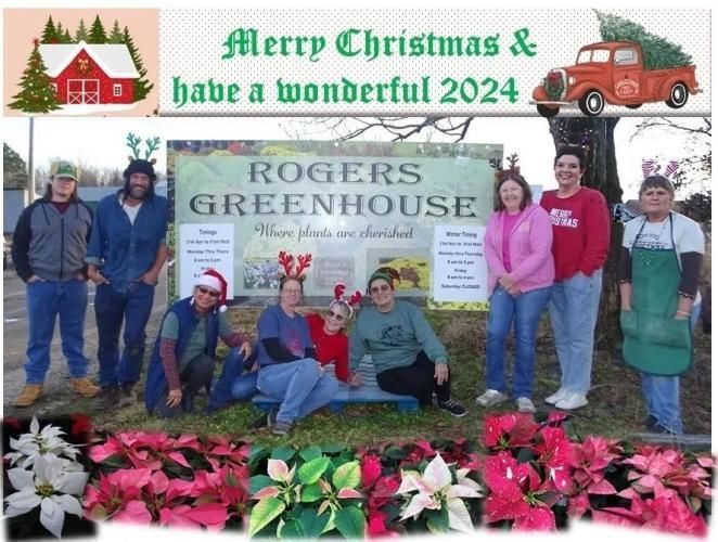 A group of employees standing and sitting in front of a Rogers Greenhouse sign during Christmas, with poinsettias in front.
