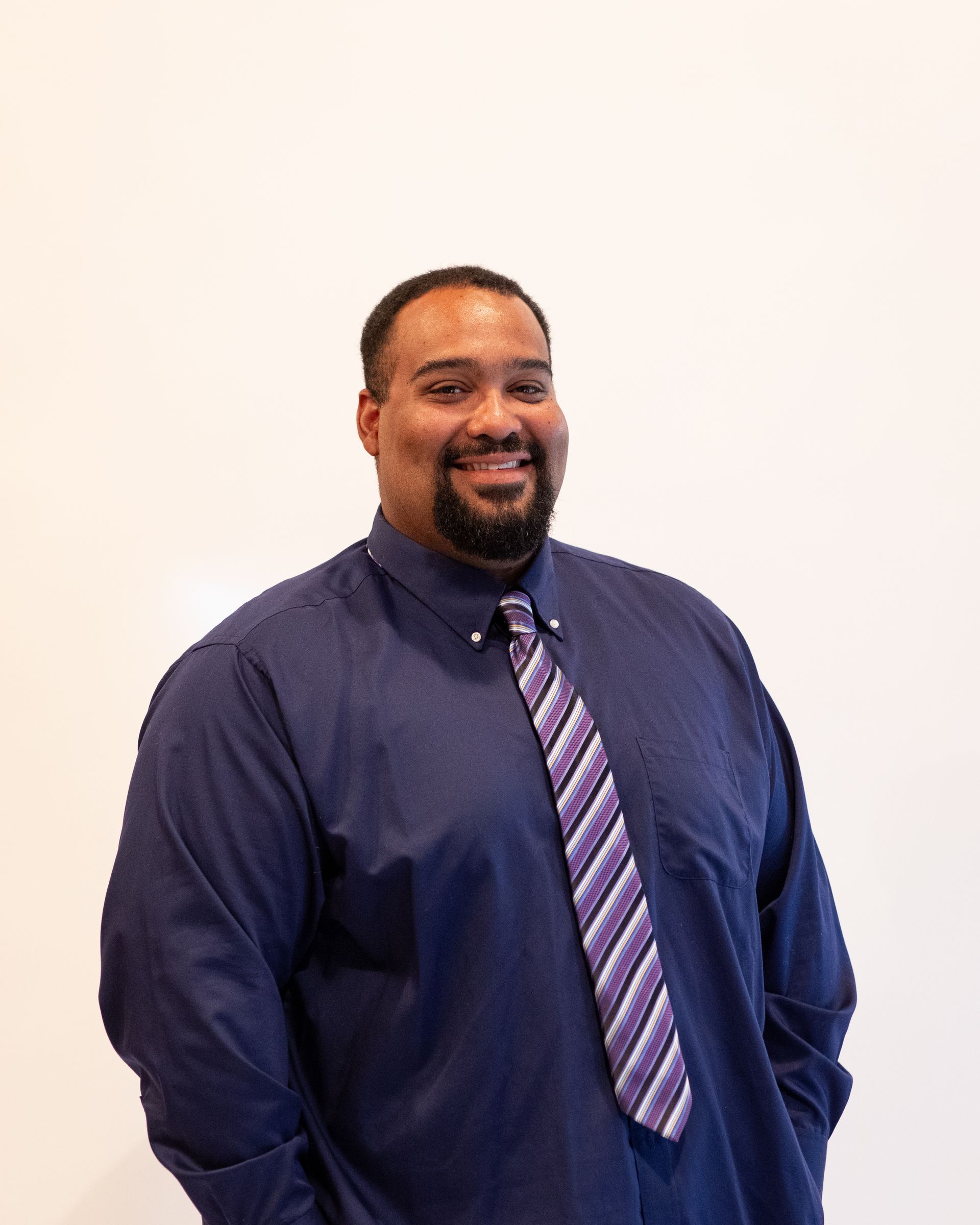 Smiling man in a navy suit and white shirt against a gray studio background