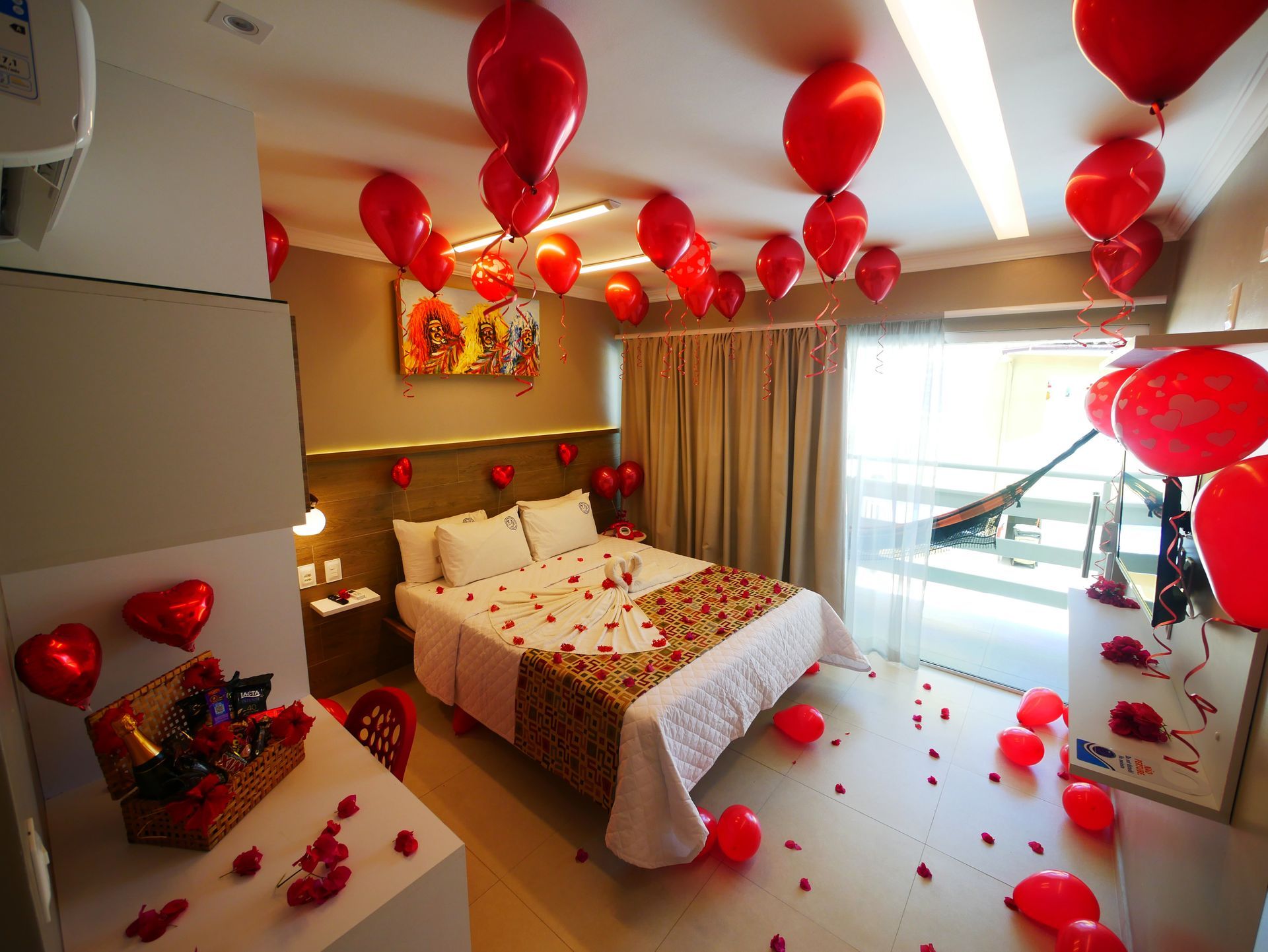Um quarto de hotel decorado com balões vermelhos e pétalas de rosa