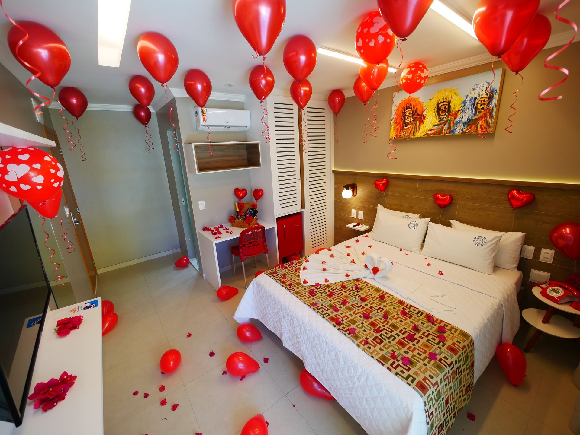 um quarto de hotel decorado para o dia dos namorados com balões e pétalas de rosa.