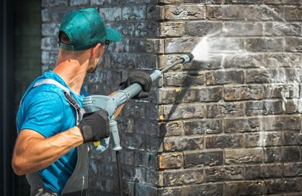 A man is cleaning a brick wall with a high pressure washer.