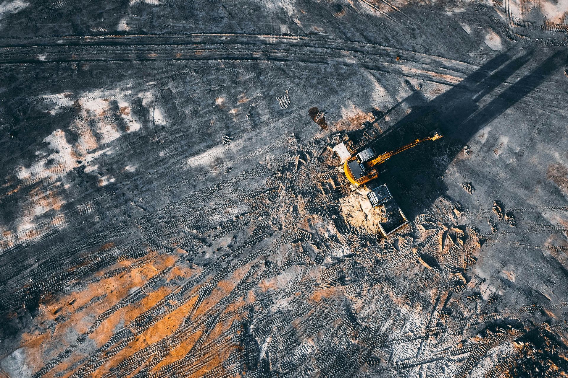 Small excavator clearing debris on a charred, ash-covered site with black smoke shadows.