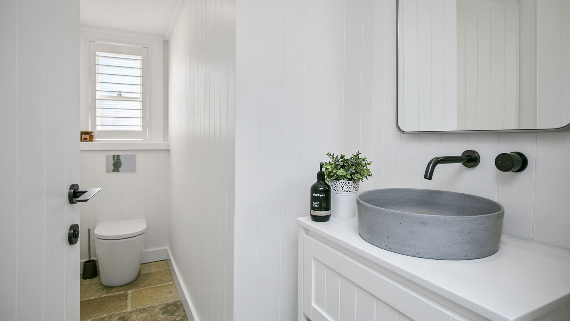 A bathroom with a toilet , sink , mirror and window.