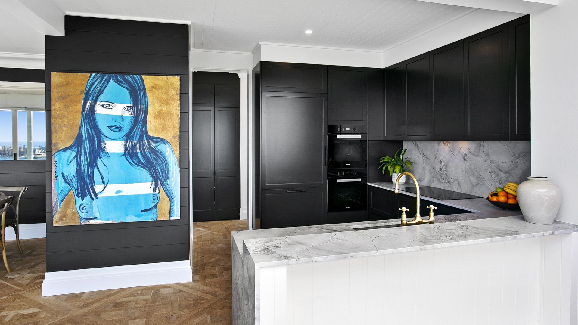 A kitchen with black cabinets and a painting of a woman on the wall.