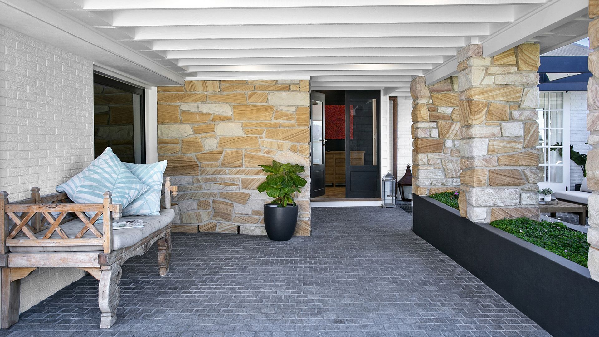 There is a bench and a potted plant on the porch of a house.