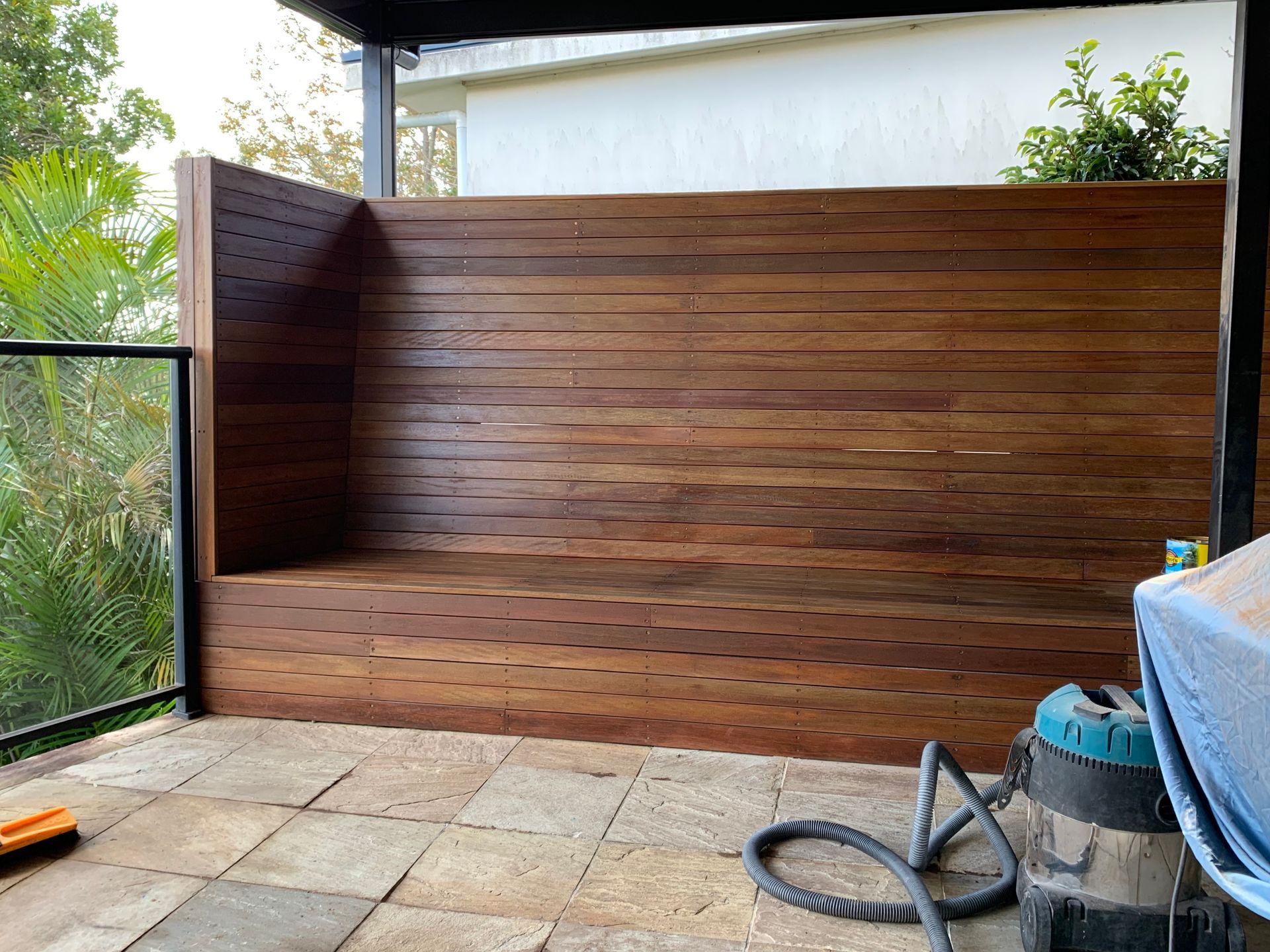 A wooden bench is sitting on a patio next to a vacuum cleaner.