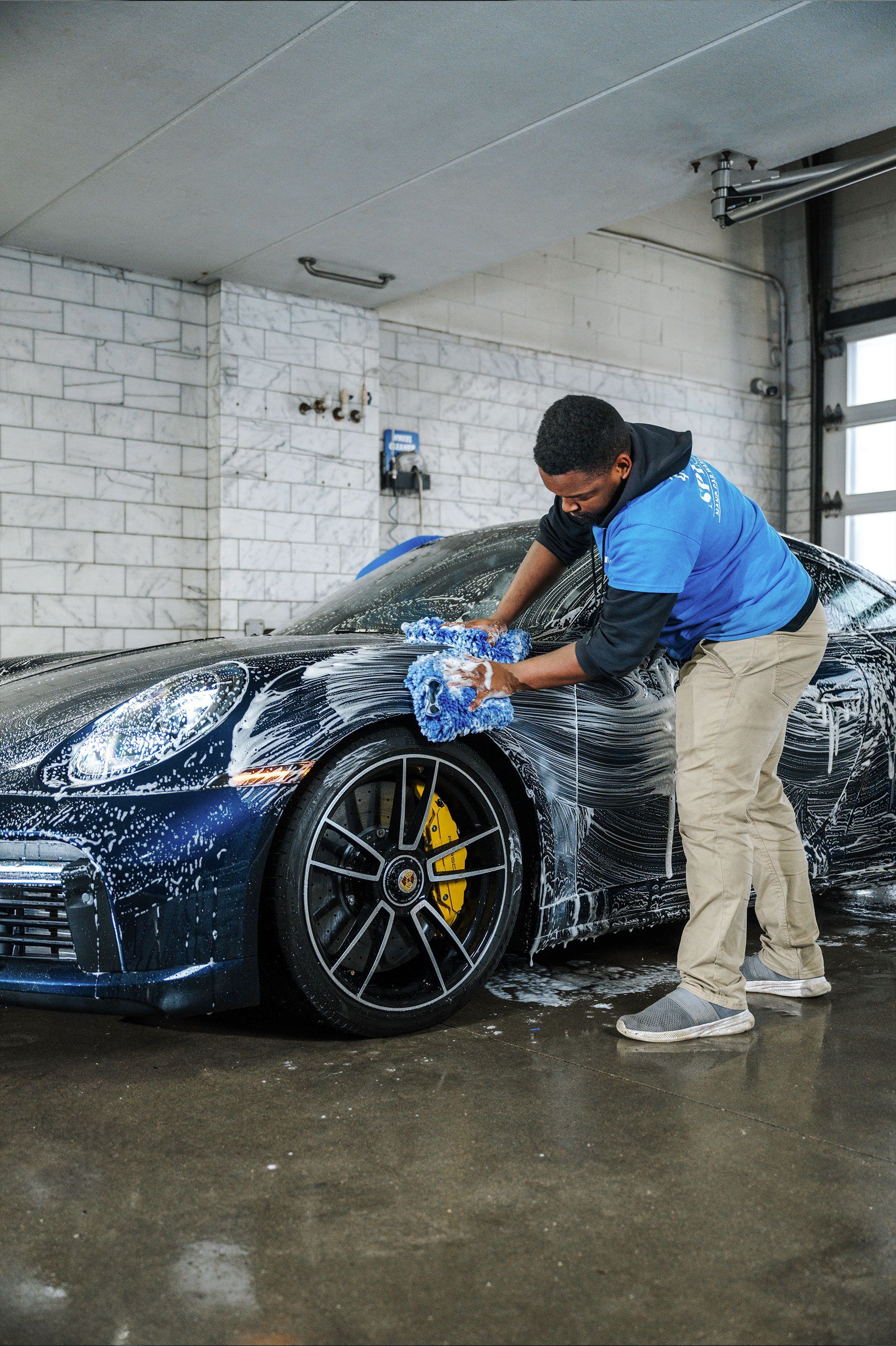 A man is washing a blue sports car in a garage.