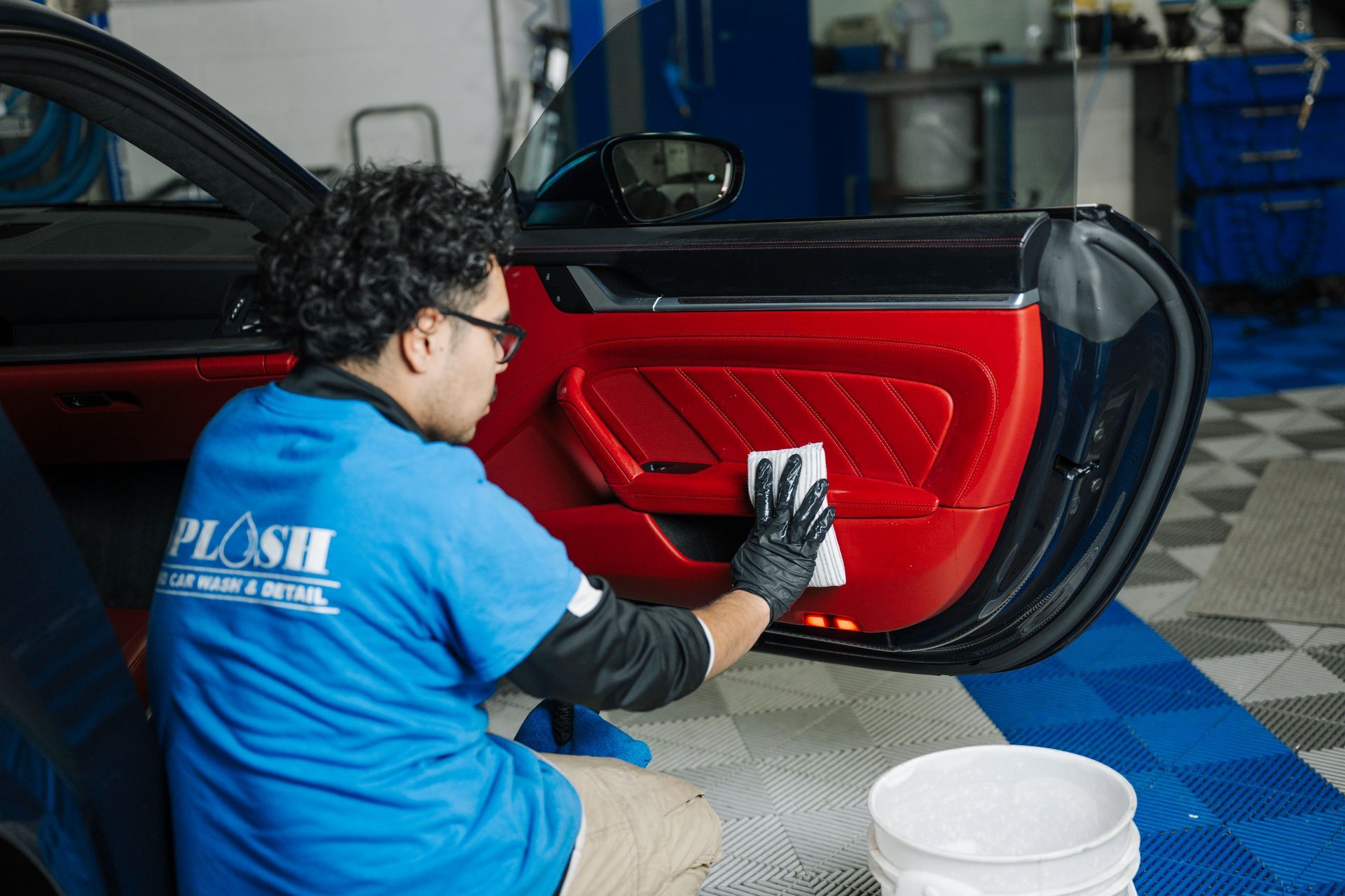 A man in a blue shirt is cleaning the door of a red car.