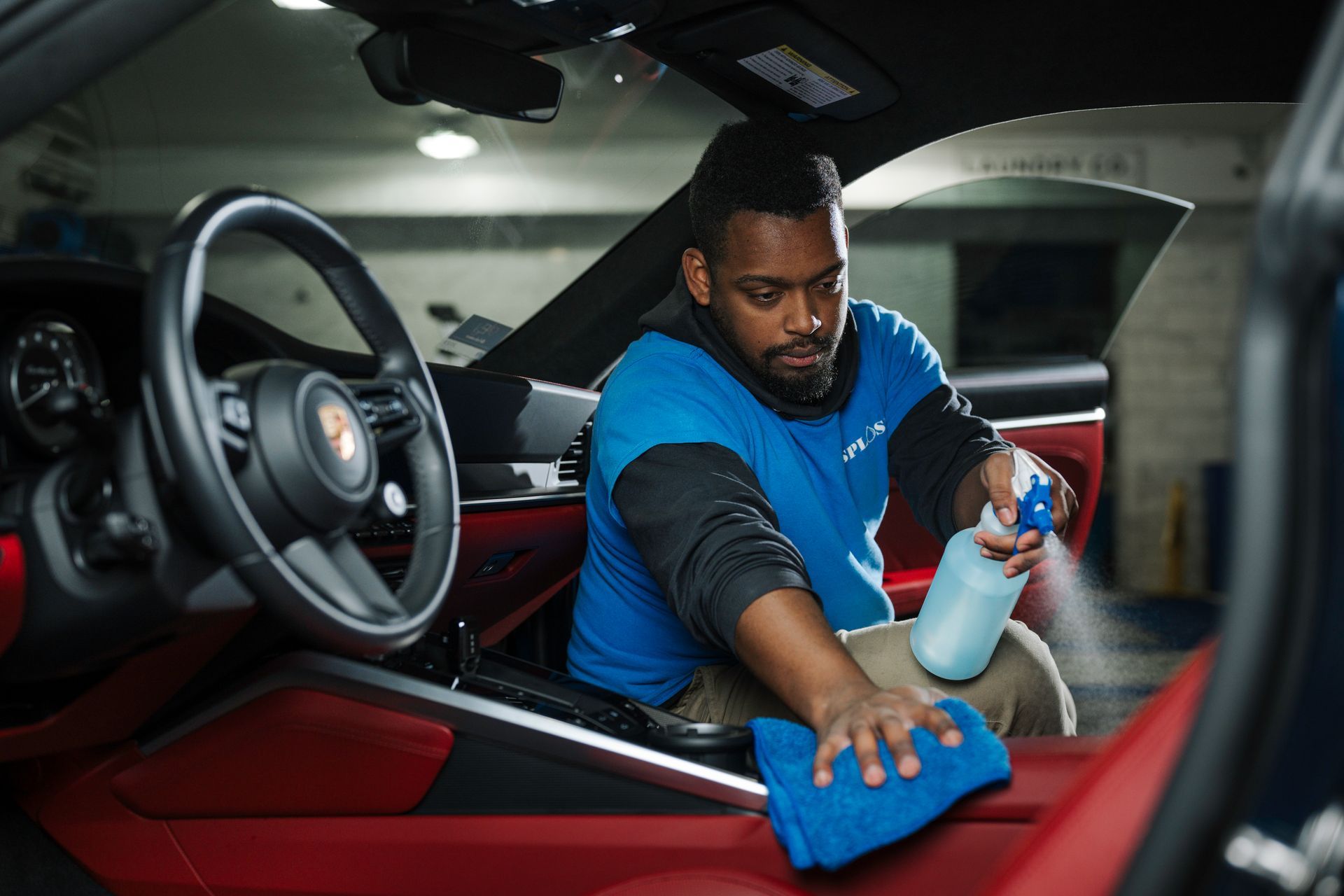 A man is cleaning the interior of a car with a cloth and spray bottle.