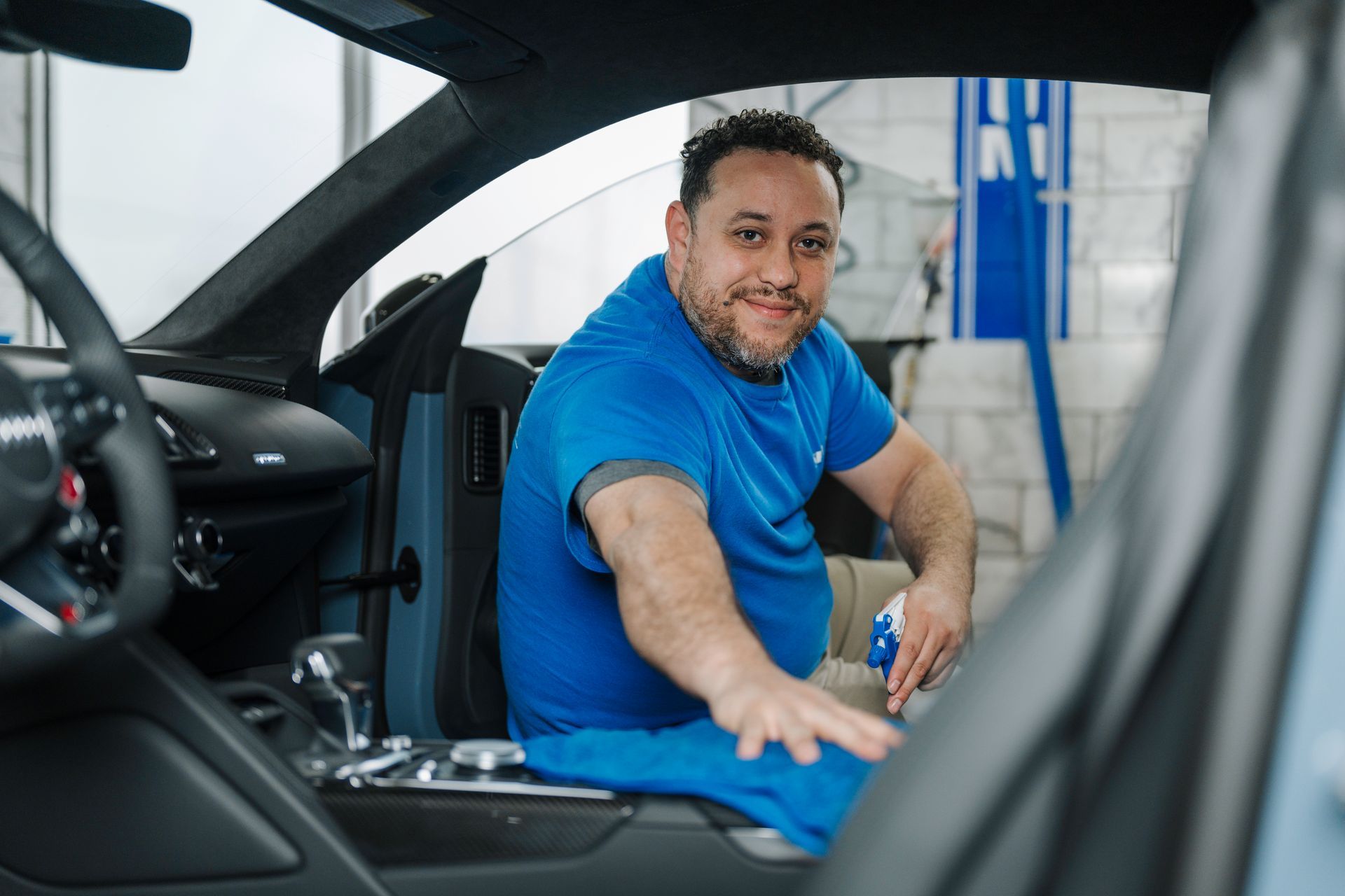 A man is sitting in the driver 's seat of a car and pointing at the steering wheel.