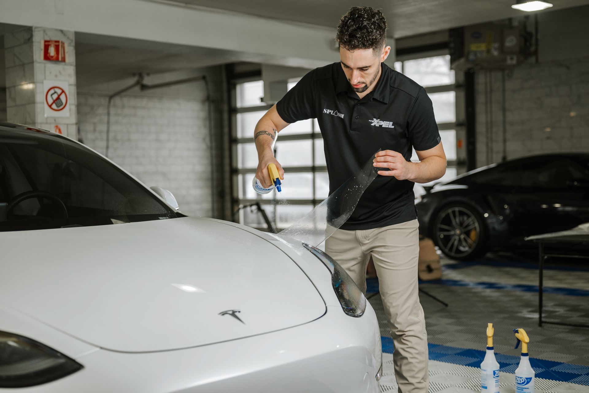 A man is installing PPF on a tesla model 3 in a garage.