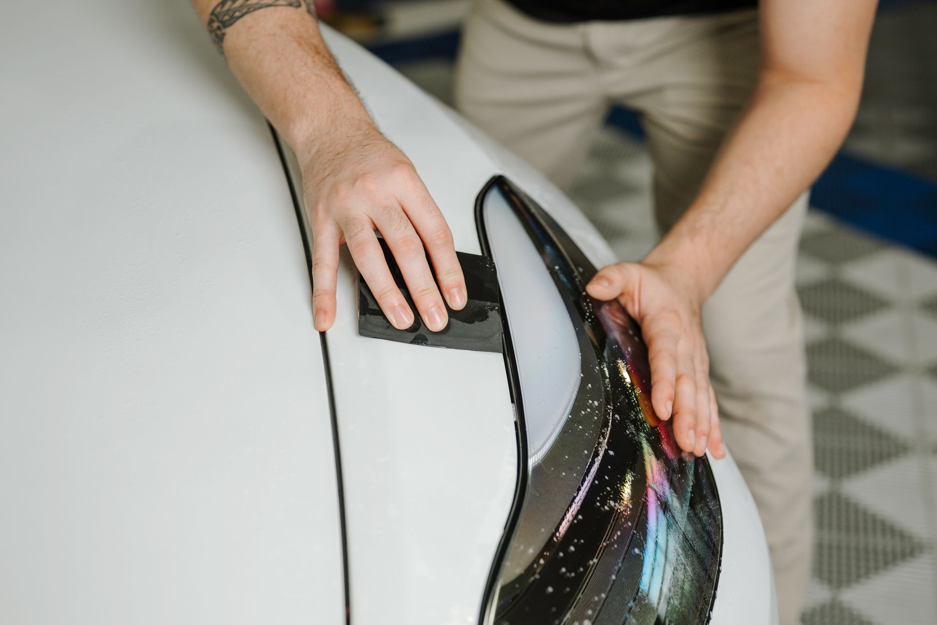 A man is polishing the headlight of a white car.