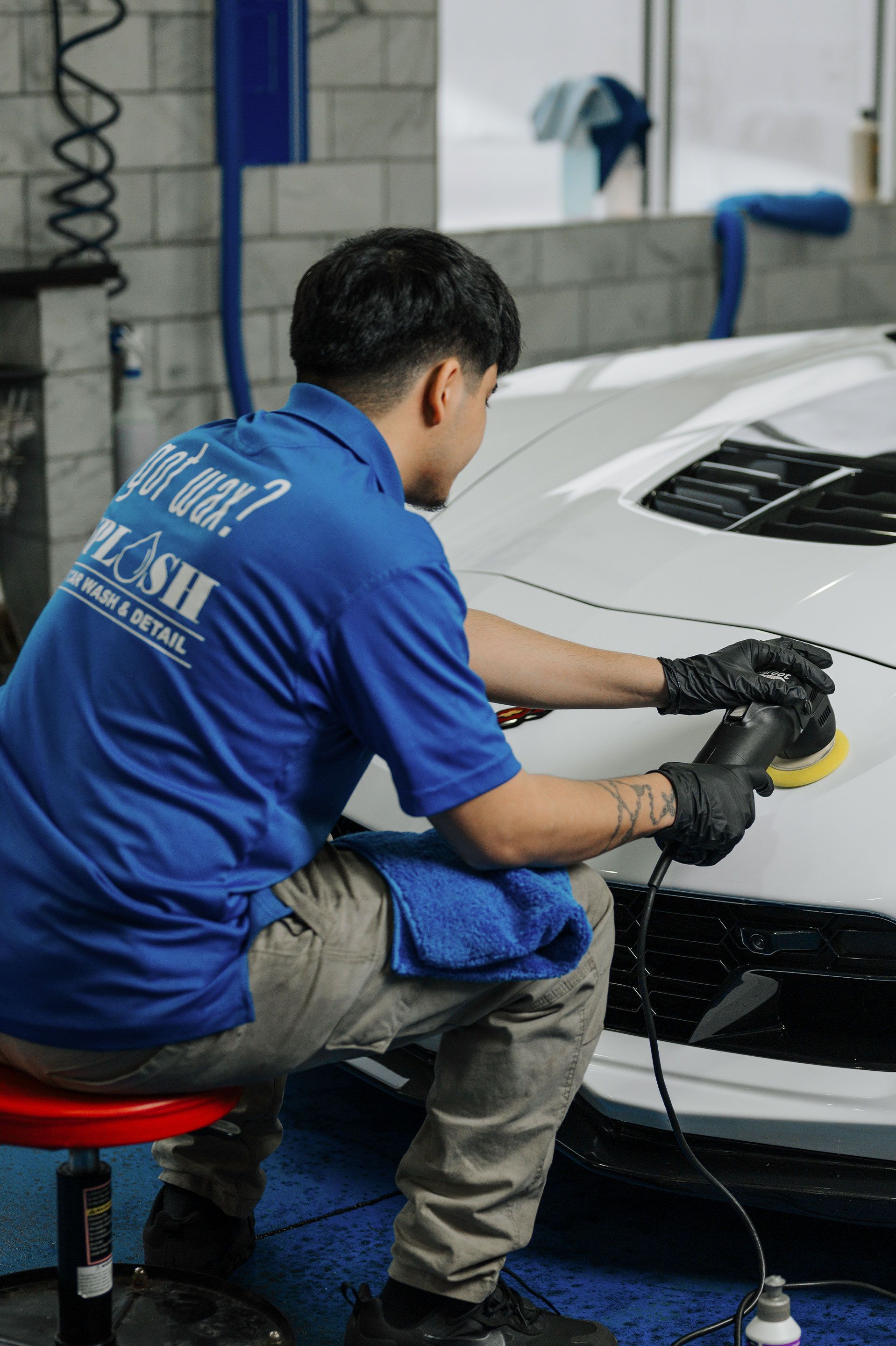 A man in a blue shirt is polishing a white car.