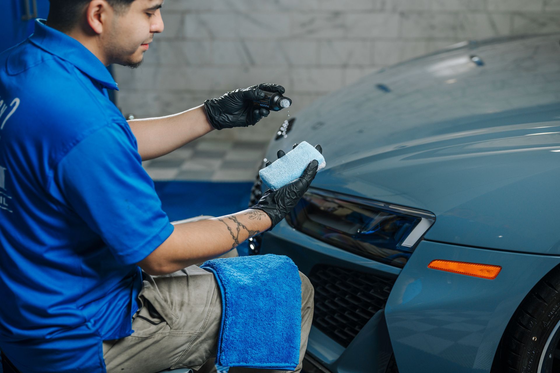 A man in a blue shirt is cleaning a car with a sponge.