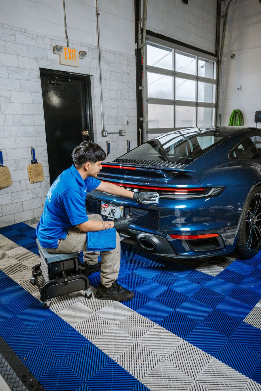 A man is sitting on a stool in front of a blue car in a garage.