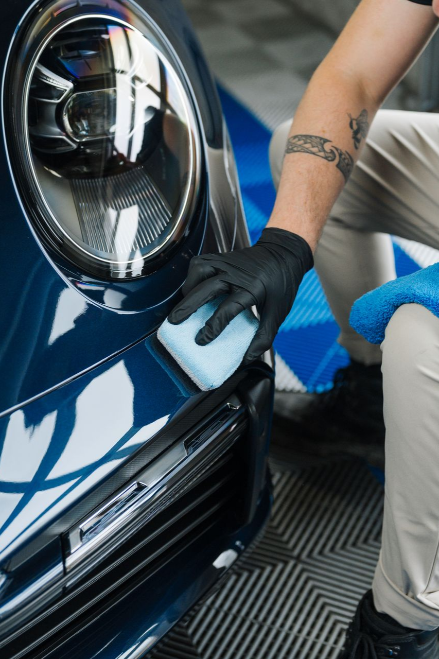 A man is polishing the front of a blue car.