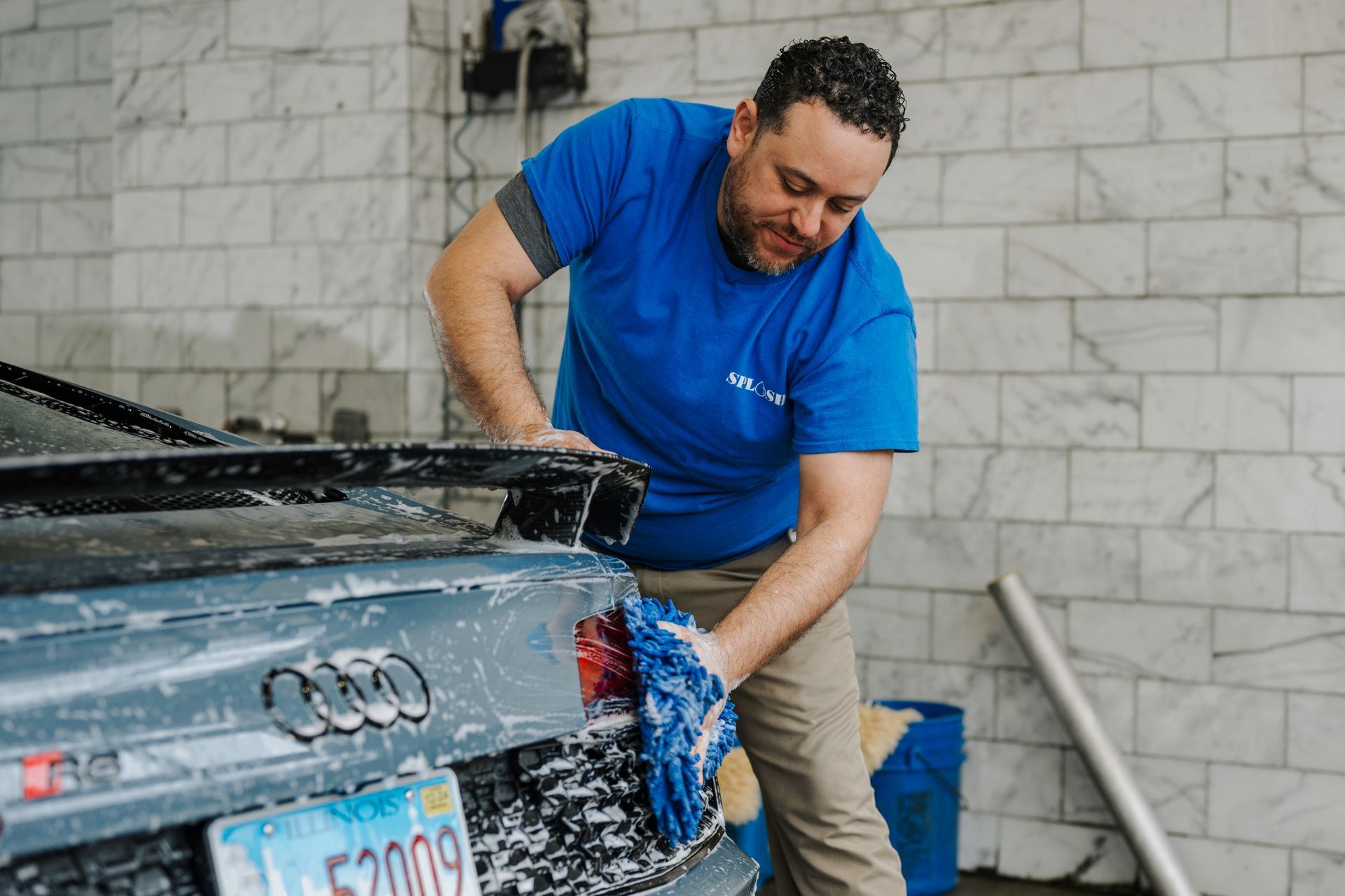 A man in a blue shirt is washing a car in a car wash.