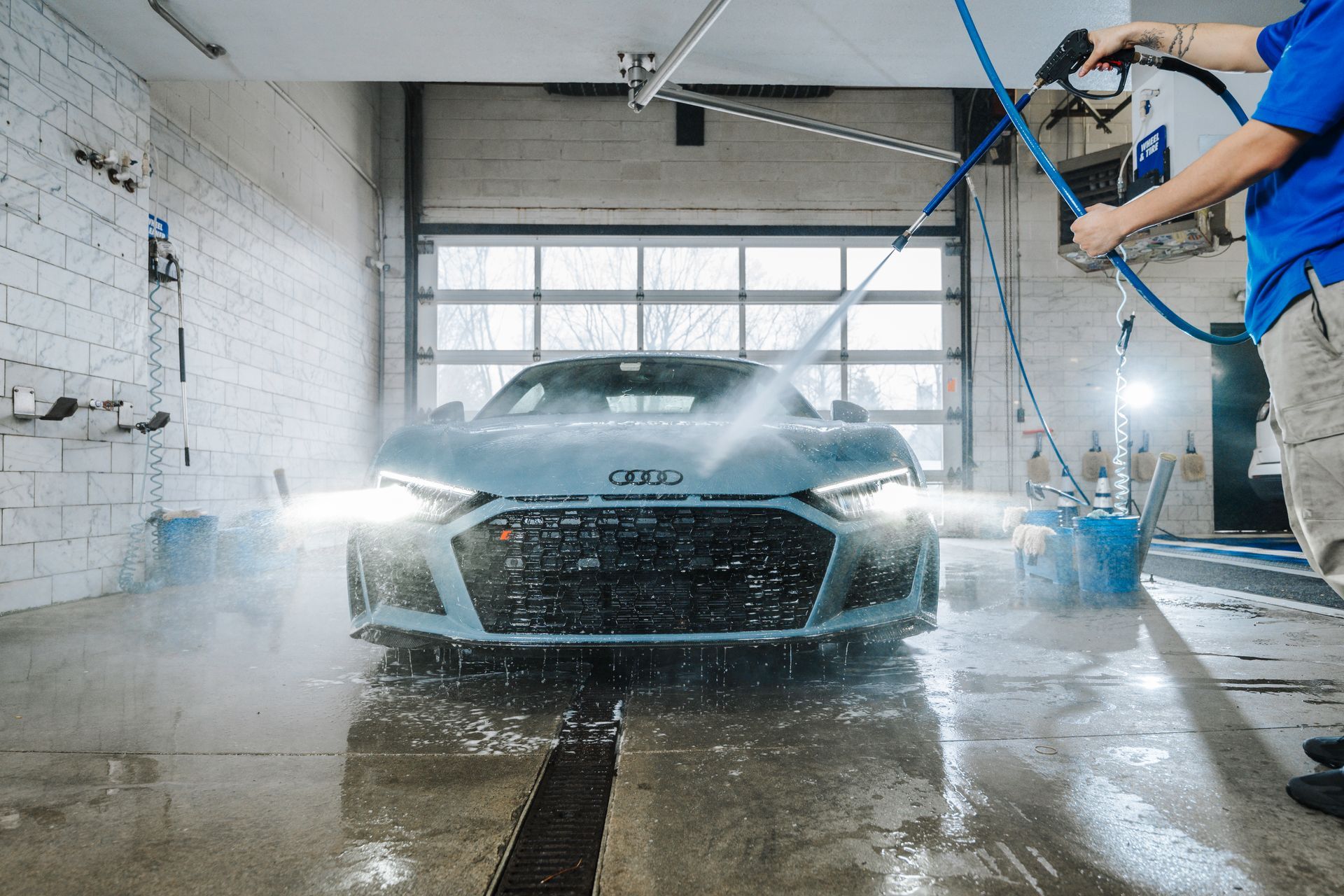 A man is washing a car in a garage with a high pressure washer.