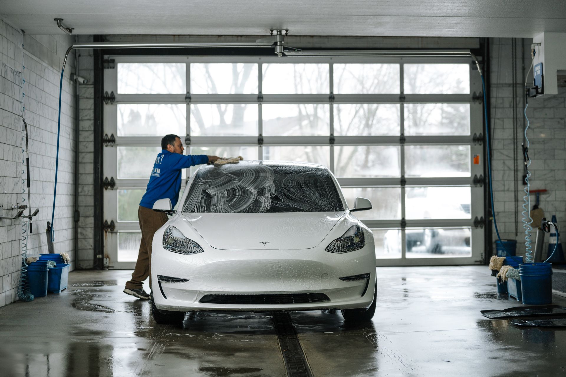 A man is washing a tesla model 3 in a garage.